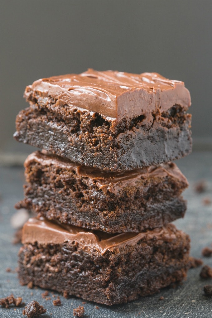 A stack of healthy flourless fudge brownies with a thick chocolate frosting on top. 