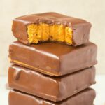 A stack of chocolate peanut butter no bake bars which are keto and paleo-friendly. The top one has a bite mark out of it.
