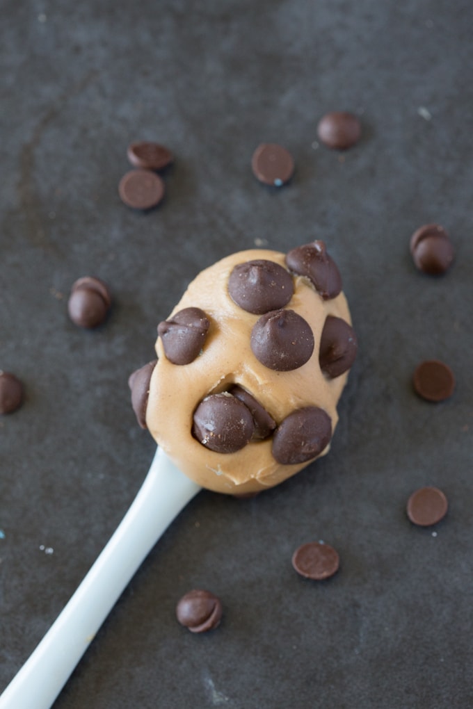 A spoonful of peanut butter topped with chocolate chips, with chocolate chips scattered in the background.