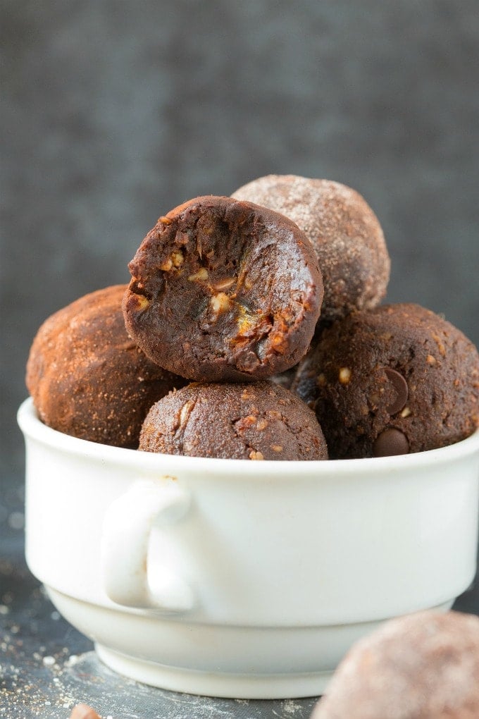 A white bowl filled with paleo whole30 no bake chocolate protein balls, with the one at the front with a bite mark out of it