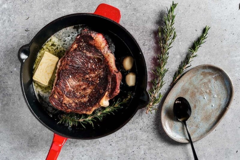 steak cooking in a cast iron skillet with butter and garlic.