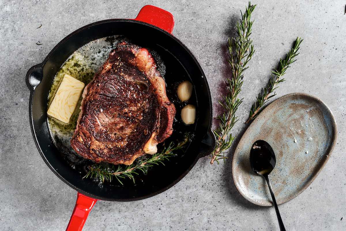 steak cooking in a cast iron skillet with butter and garlic.