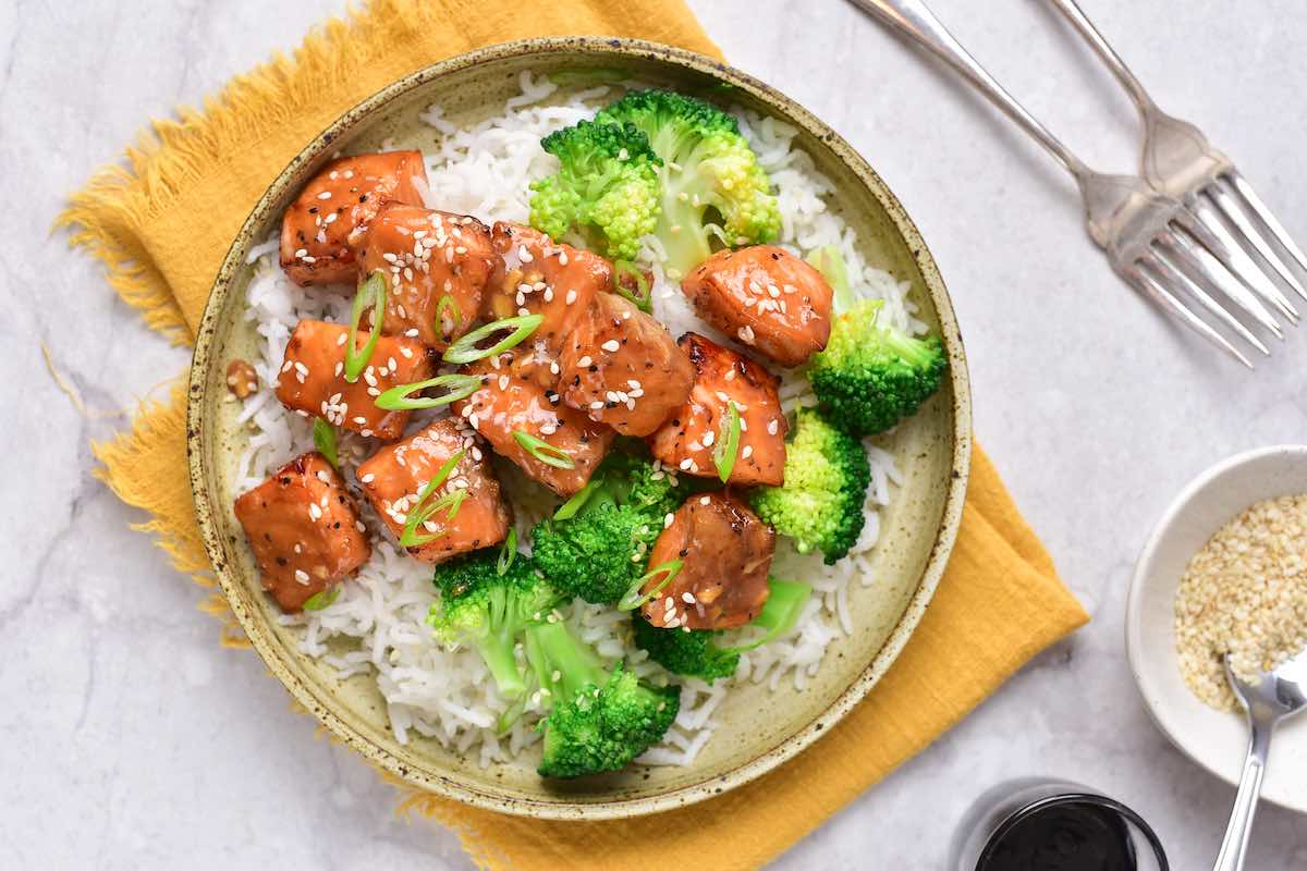 sauce drizzled on salmon bites in a bowl with rice. 