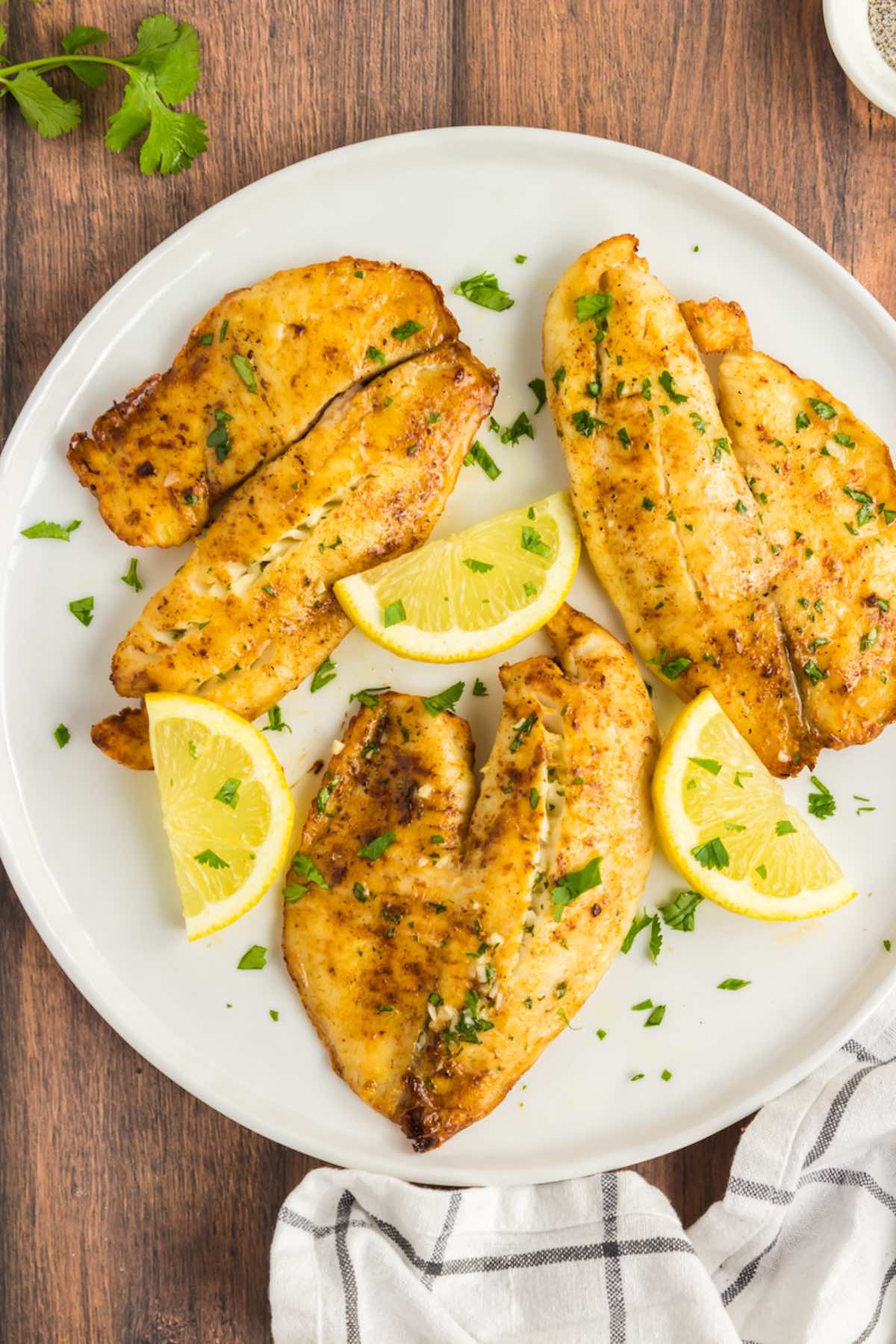 air fryer tilapia on a plate with lemon wedges.