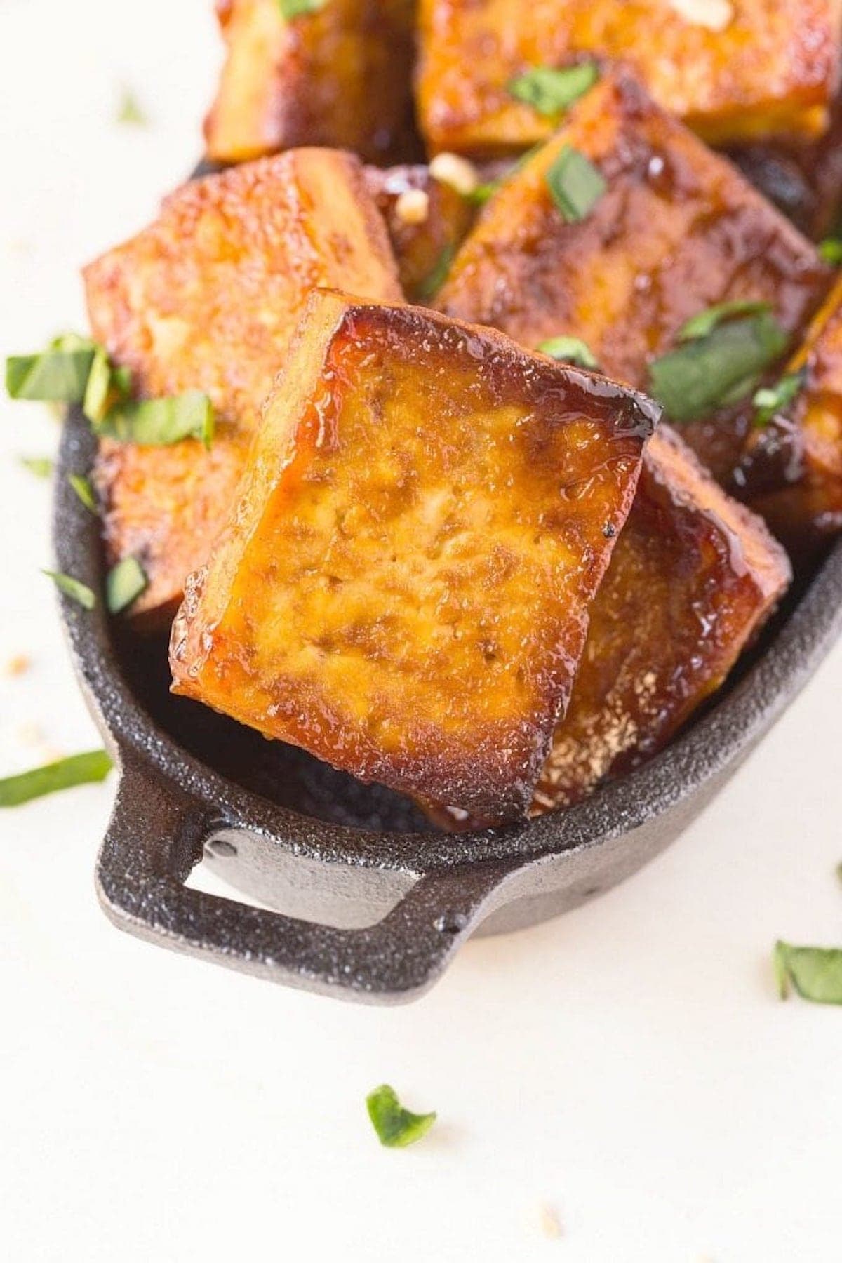 barbecue tofu in a skillet with chopped herbs.