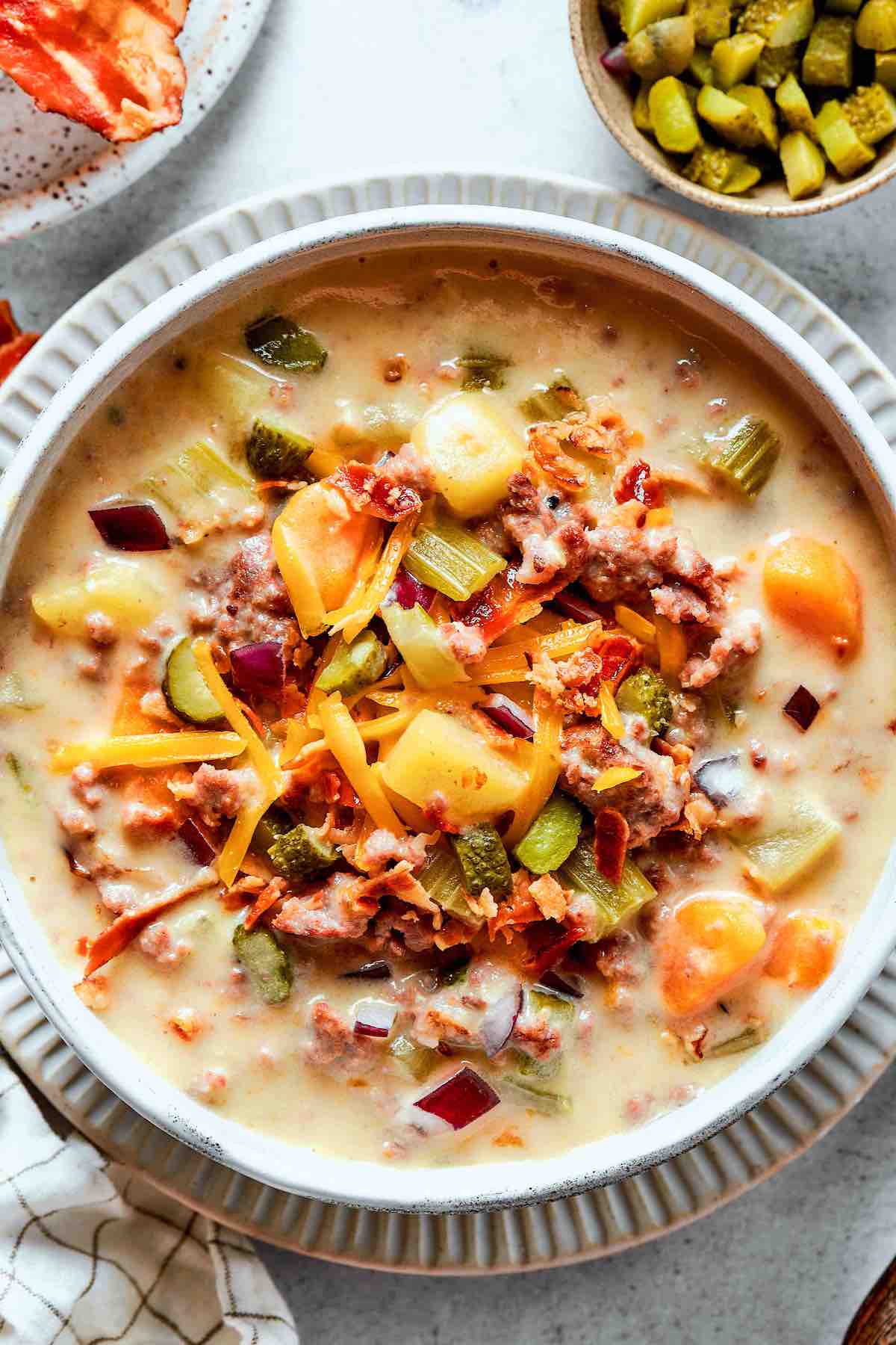 cheeseburger soup with bacon and pickles on top.