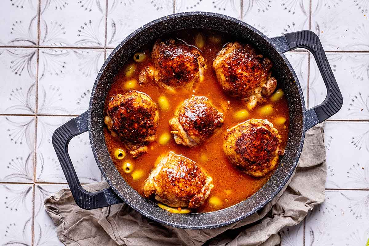 chicken thighs simmering in broth in a skillet.