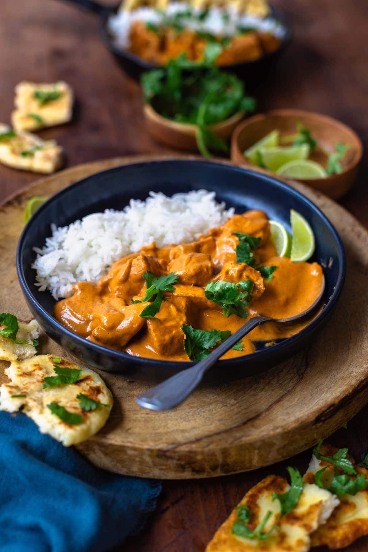 chicken masala in a bowl with rice and chopped parsley on top.