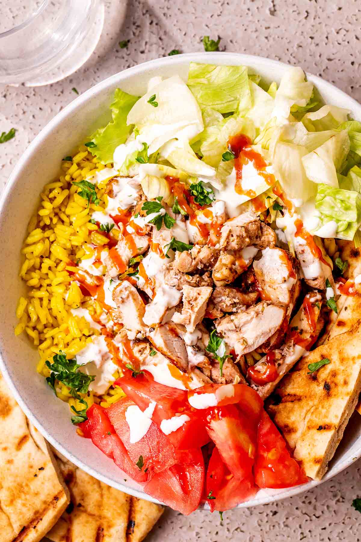 chicken over rice with tomatoes, lettuce, yogurt sauce, and pita bread.