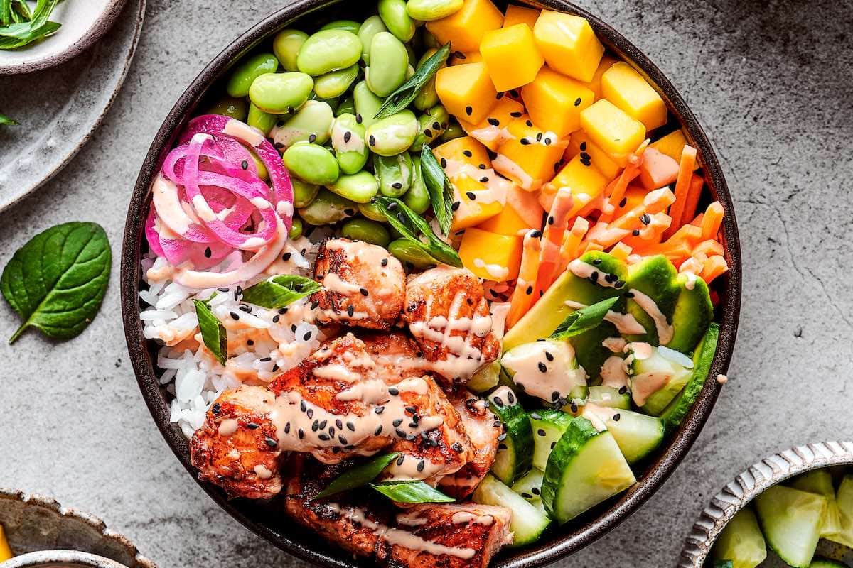 salmon bowl with spicy mayo, edamame, mango, pickled onions, and cucumbers over rice. 