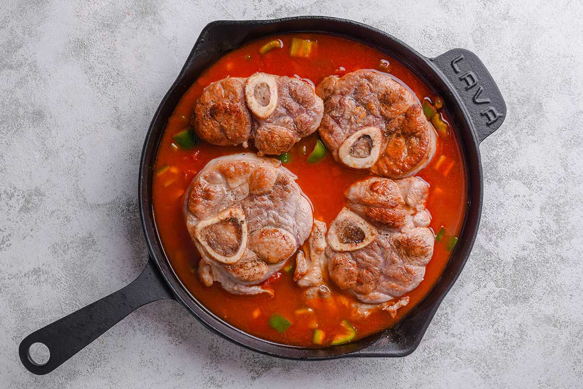 raw veal shanks in skillet with sauce.