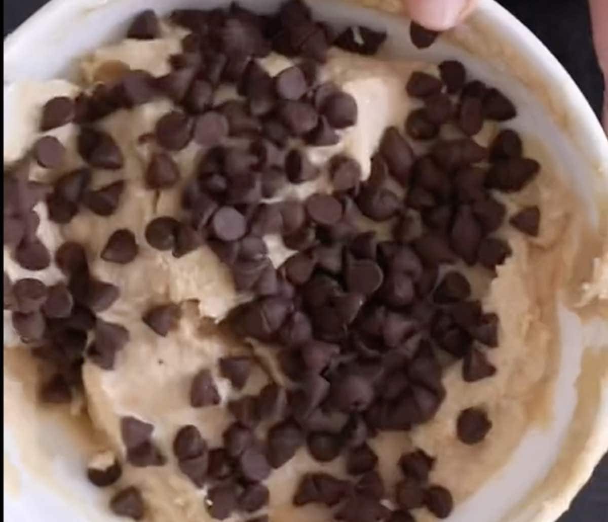 Adding chocolate chips to protein muffin batter in a mixing bowl.
