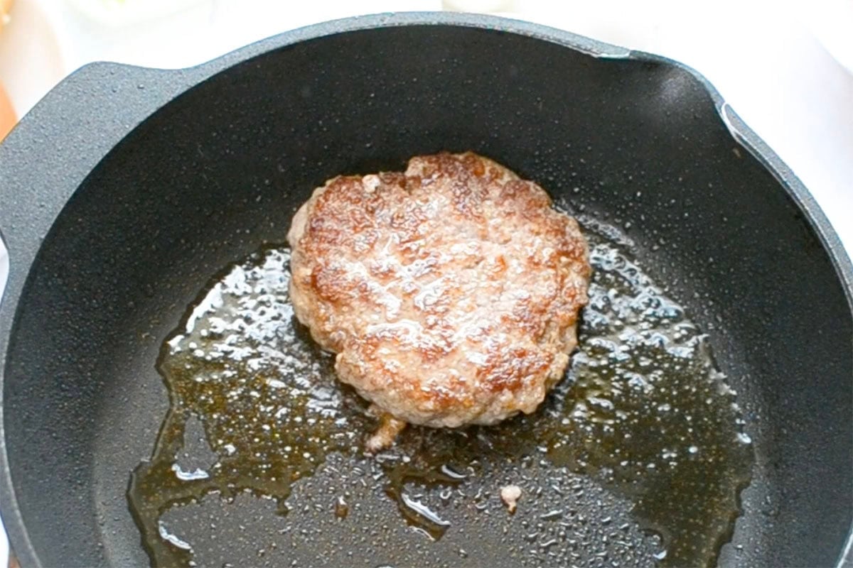 sausage patty frying in a skillet.