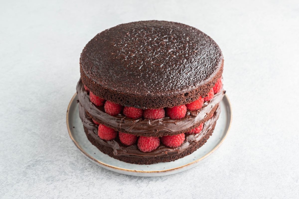layering chocolate cake with frosting and fresh raspberries.