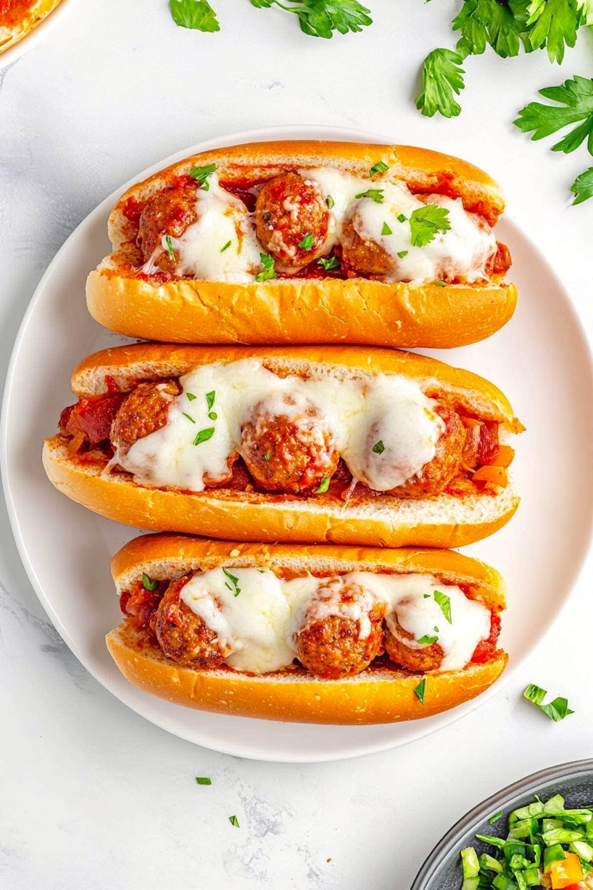 plate of meatball subs with chopped parsley on top.