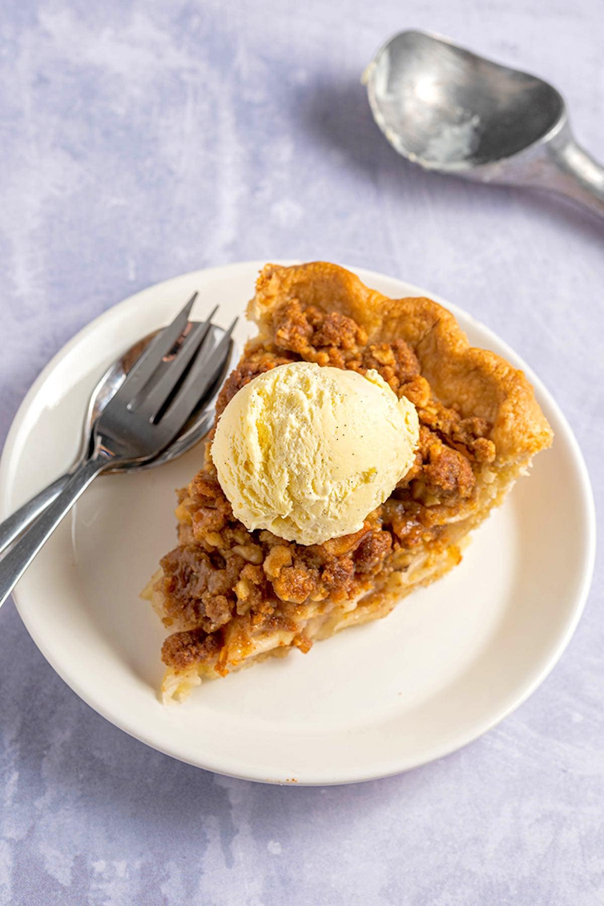 slice of apple pie with crumb topping with vanilla ice cream on top.