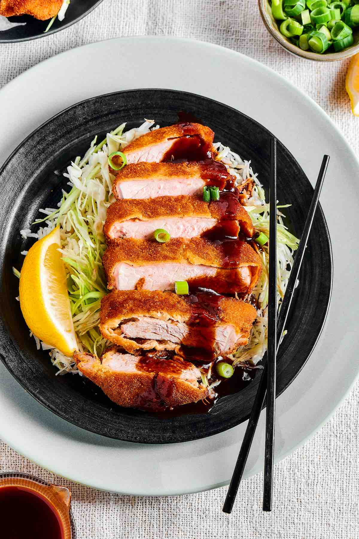 crispy pork katsu on a plate of shredded cabbage and drizzled with katsu sauce. 