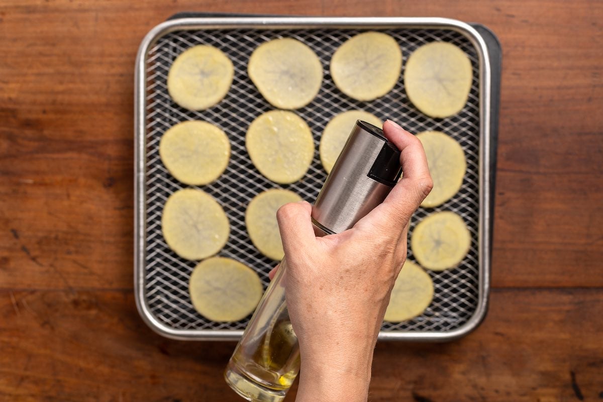 potato slices on air fryer with cooking spray on top.