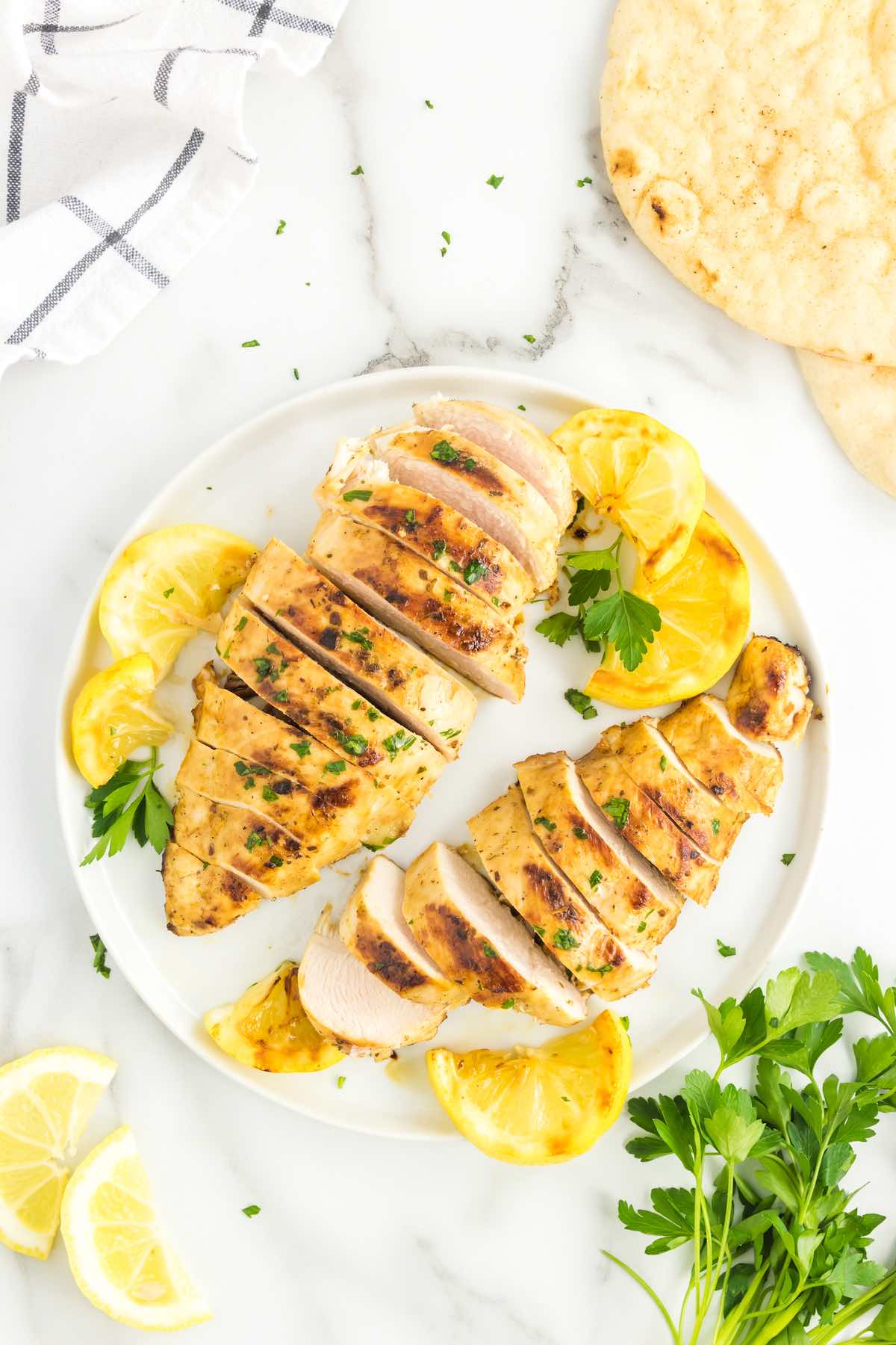 Greek chicken with fresh lemon wedges on a plate.