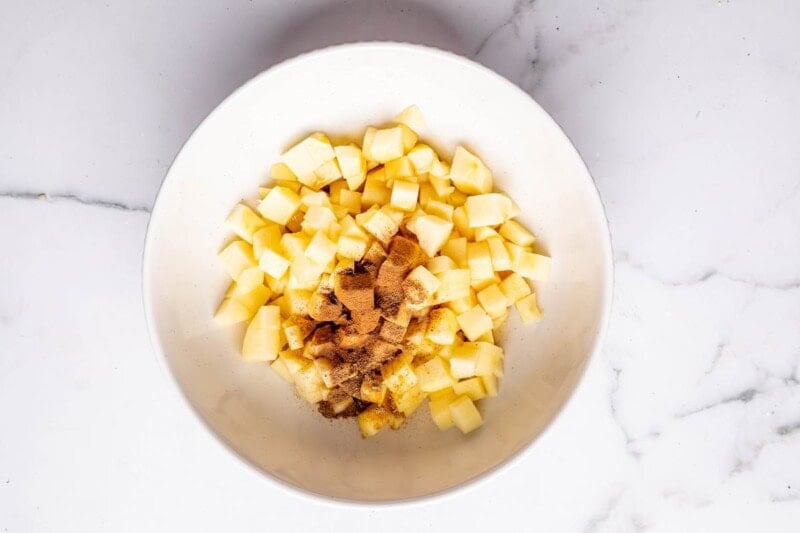 chopped apples in a bowl with cinnamon, maple syrup, and spices.