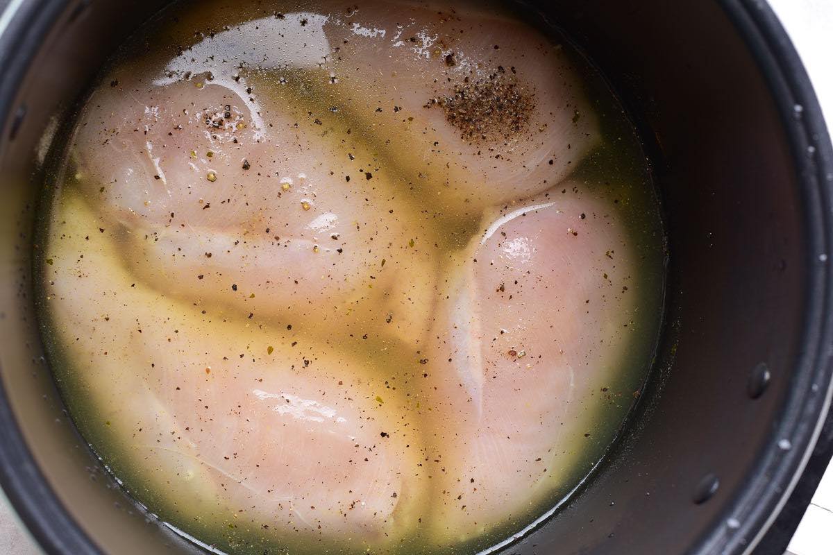 raw chicken breasts with chicken broth and seasonings in instant pot.