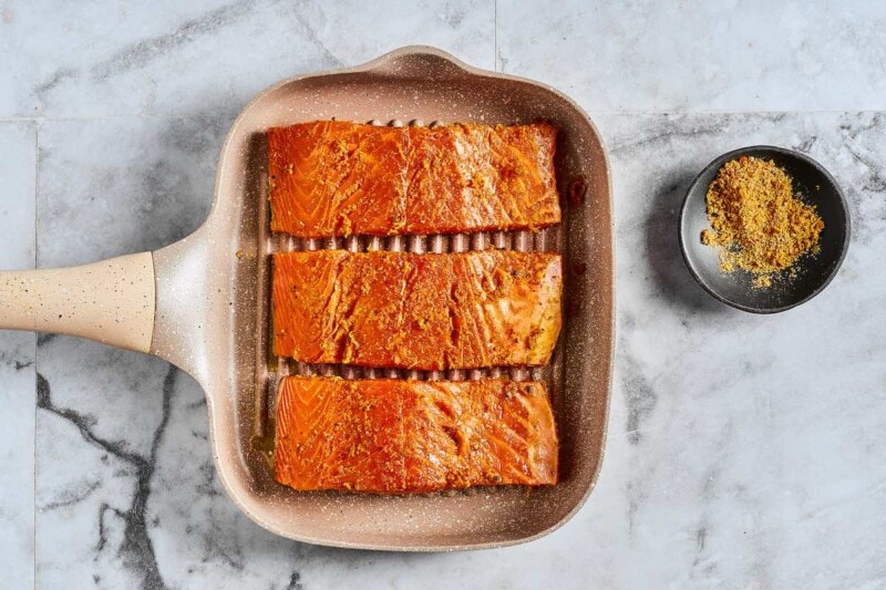 salmon fillets cooking in a skillet.