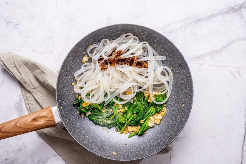 pad see ew noodles in a skillet with broccoli and egg.