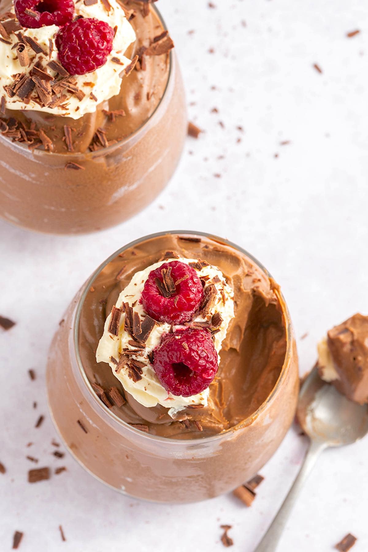 homemade avocado chocolate mousse with whipped cream and raspberries on top.