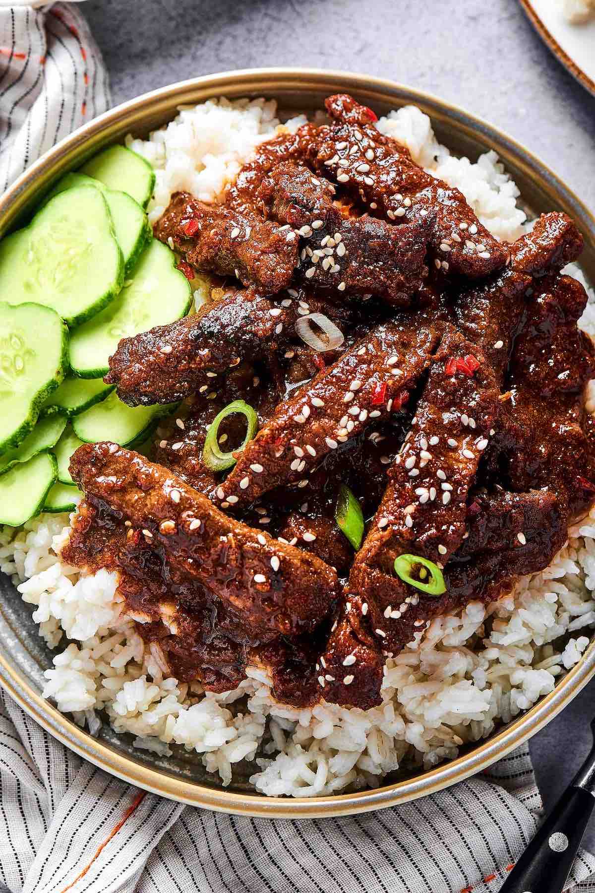 beef bulgogi over rice with sliced cucumbers.