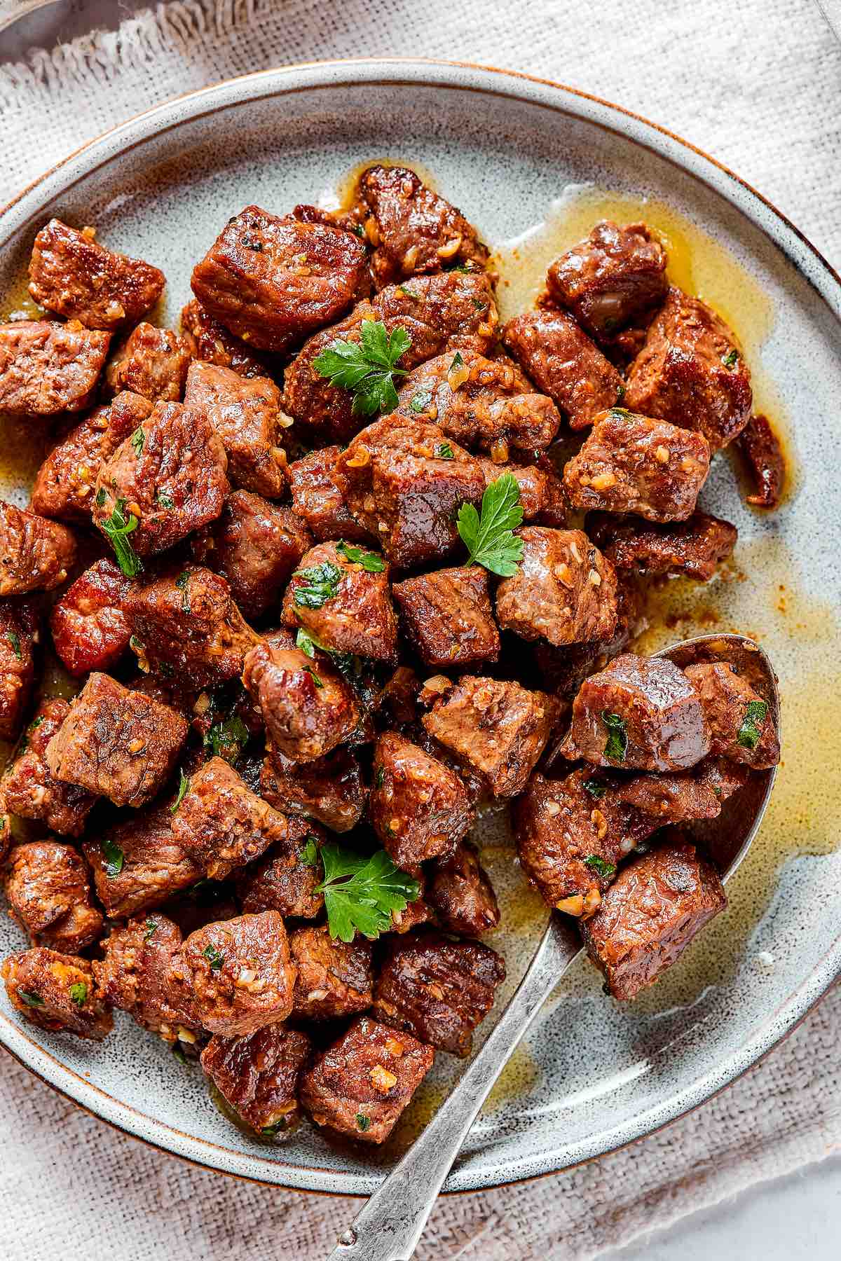 plate of garlic butter steak bites with fresh parsley on top.