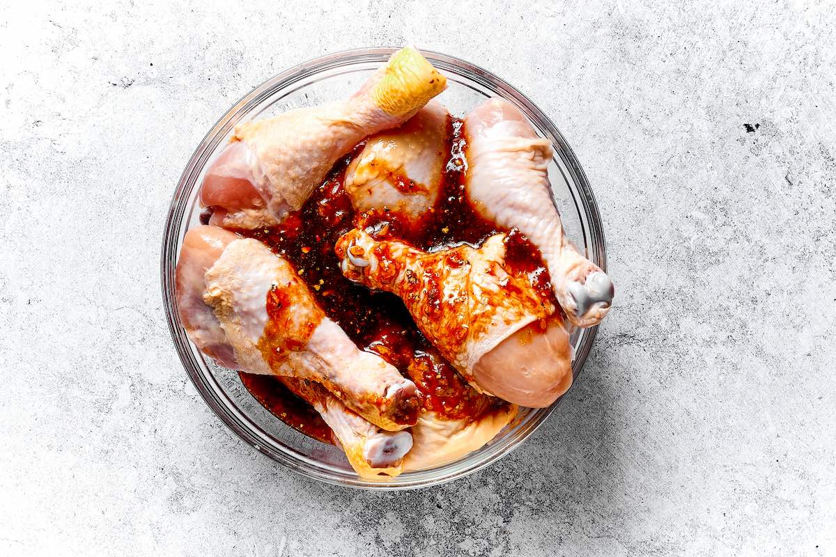 raw chicken legs in a bowl with marinade.