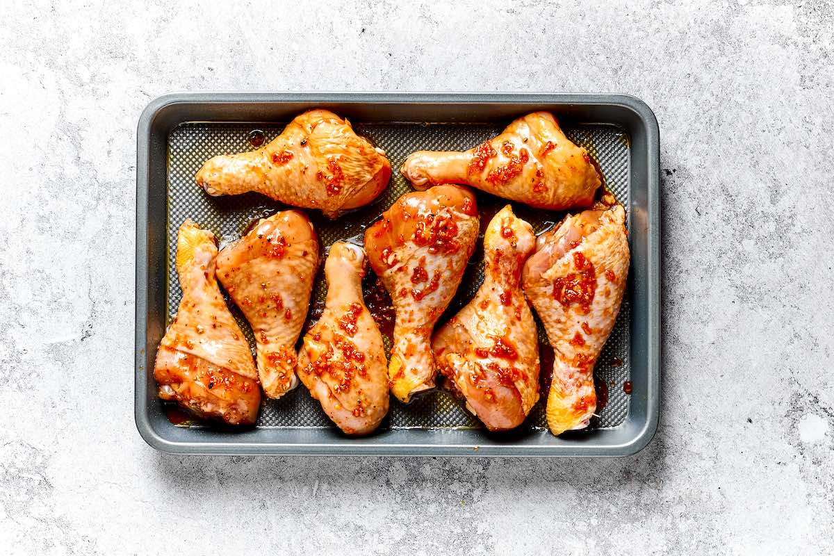 raw seasoned chicken legs on a baking dish.