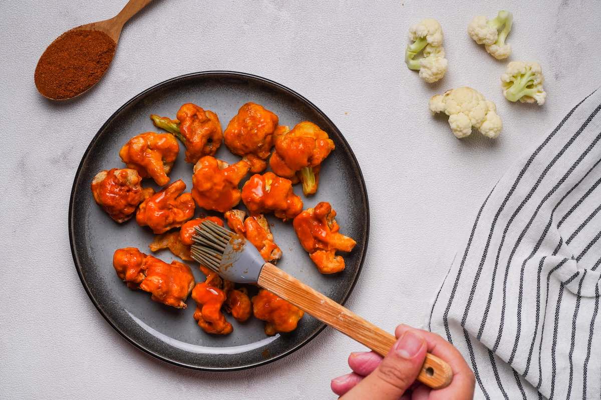 brushing battered cauliflower with buffalo sauce.