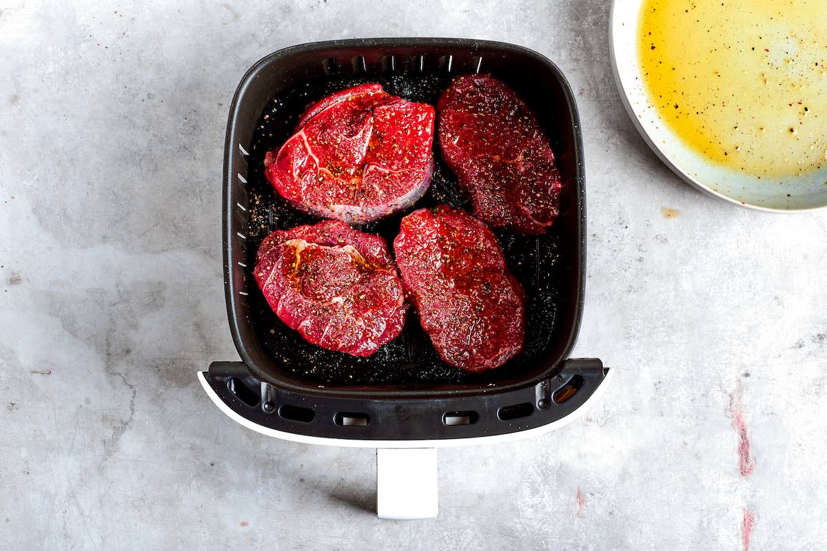 raw filet mignon steaks in the air fryer basket.