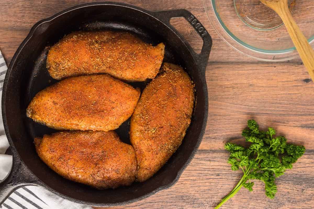 raw seasoned chicken breasts in a skillet.