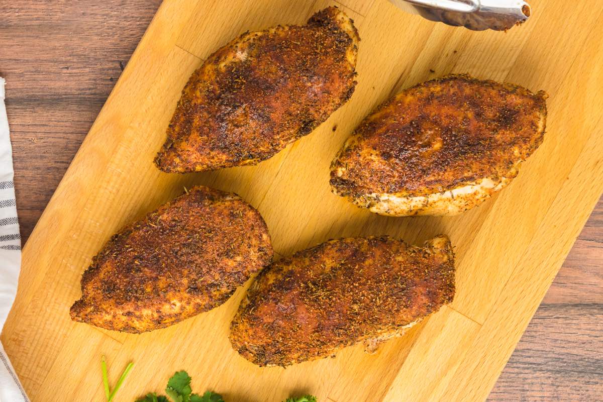 blackened chicken breast fillets on a wooden board.