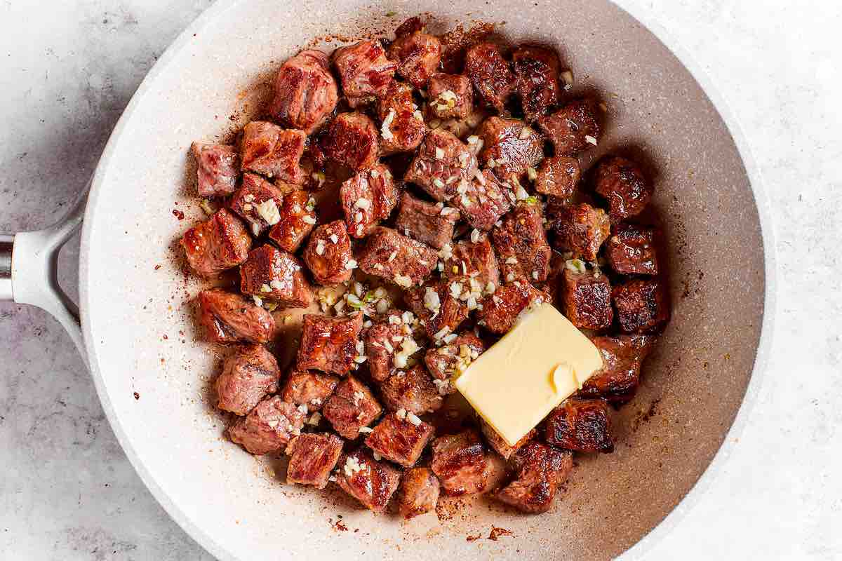 seared steak with garlic and butter on top.