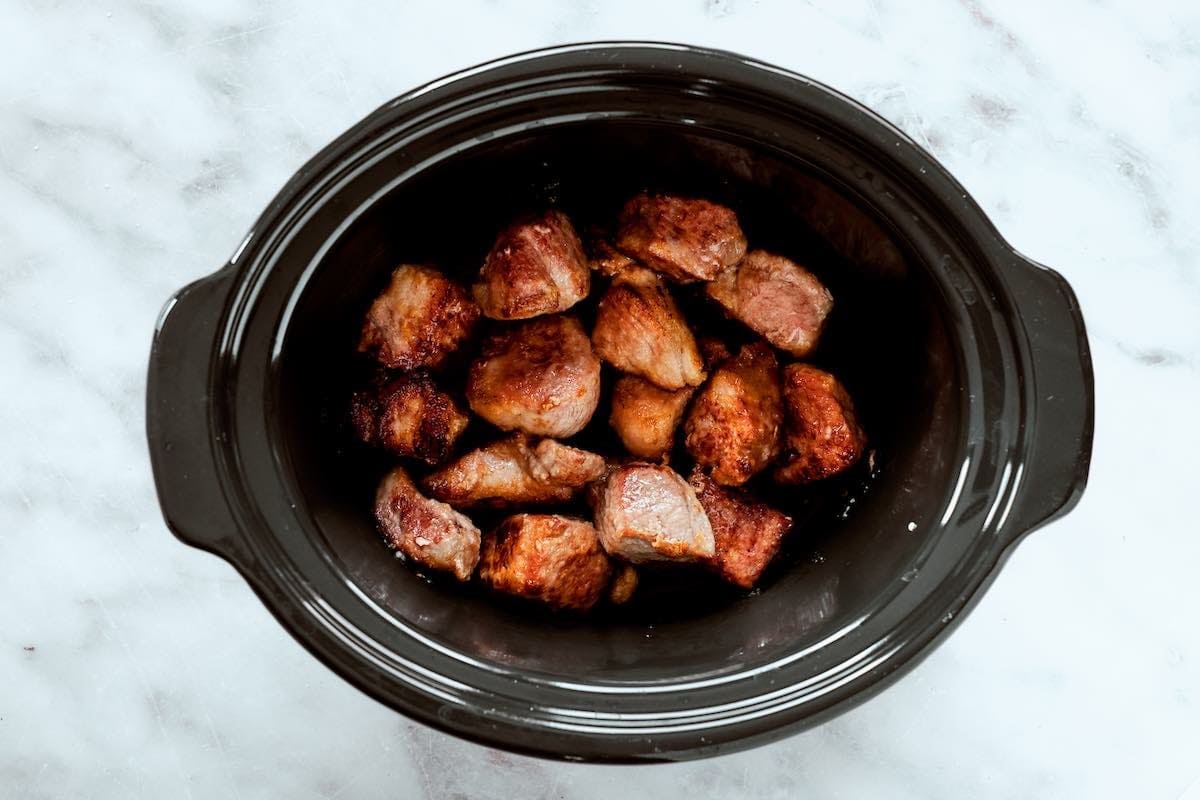 seared pork with seasonings and sauce in a slow cooker.