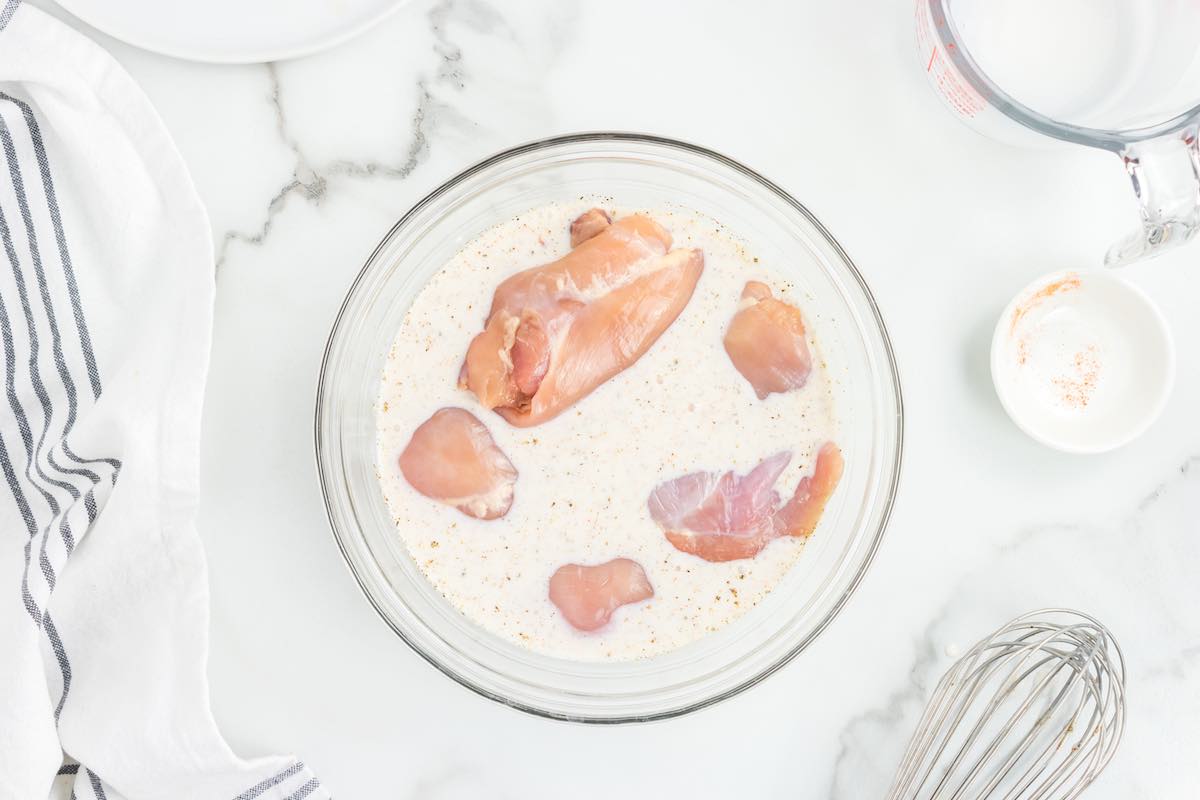 raw chicken marinated in a bowl of buttermilk.