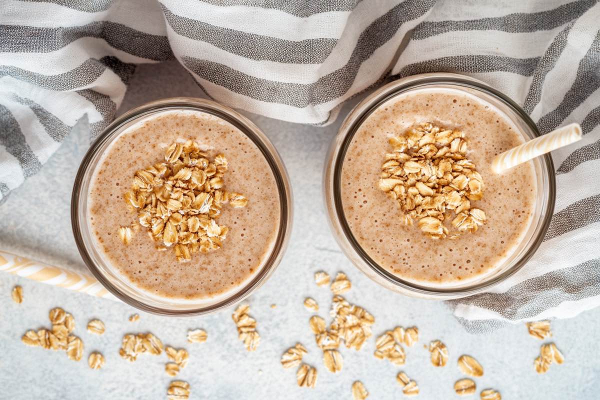 two glasses with oat smoothie and rolled oats on top.