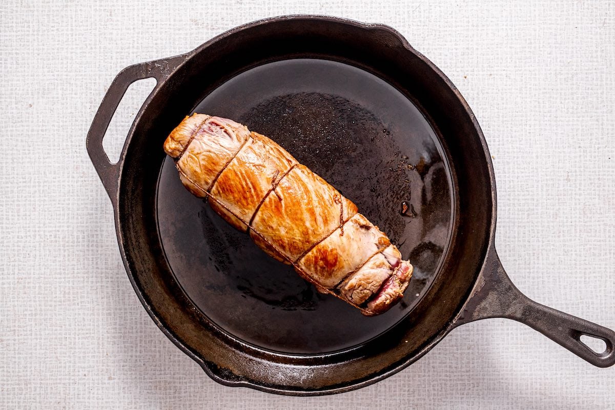 searing wrapped pork loin in a skillet.