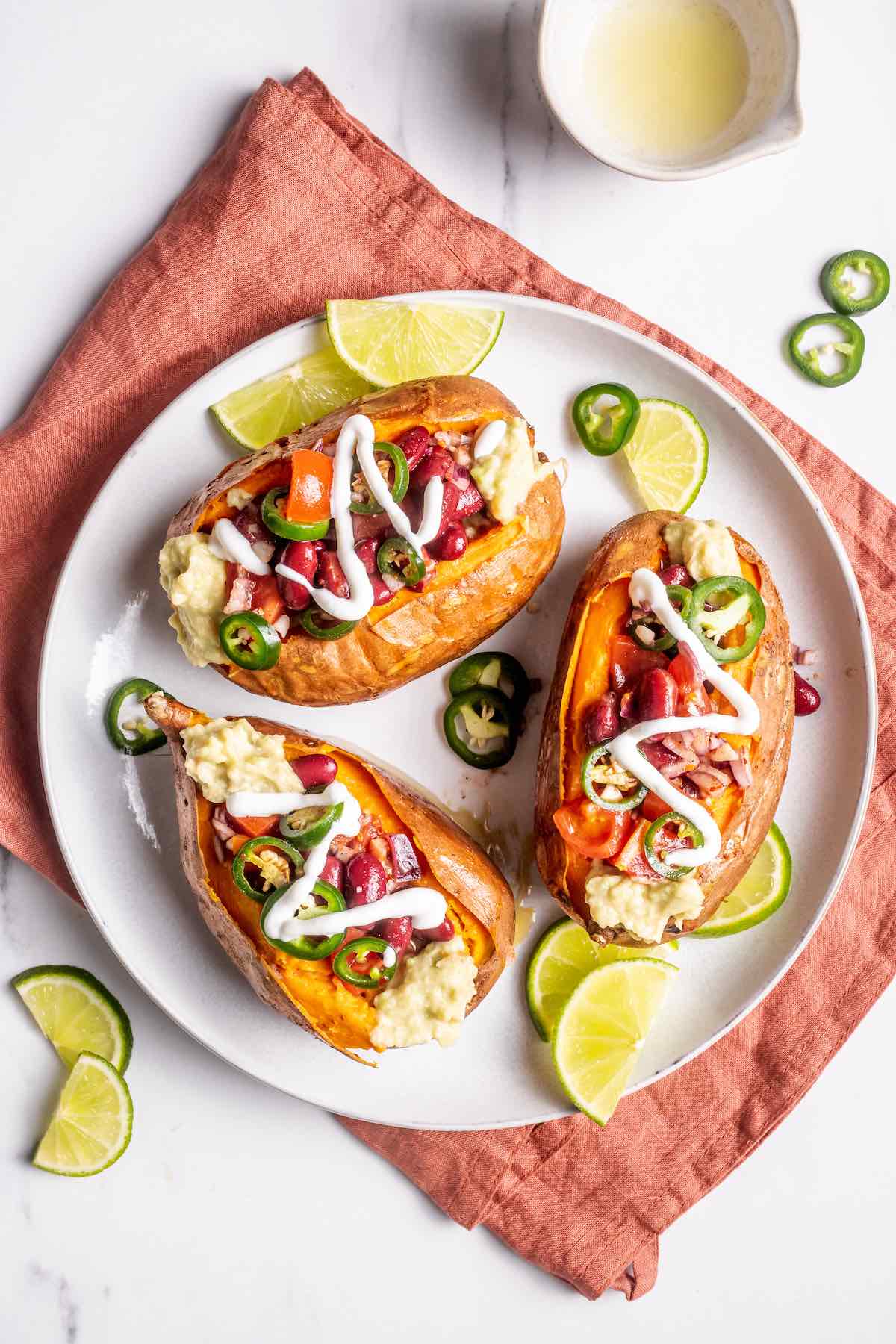 stuffed sweet potatoes on a plate with red kidney beans, guacamole, sour cream, and jalapenos.