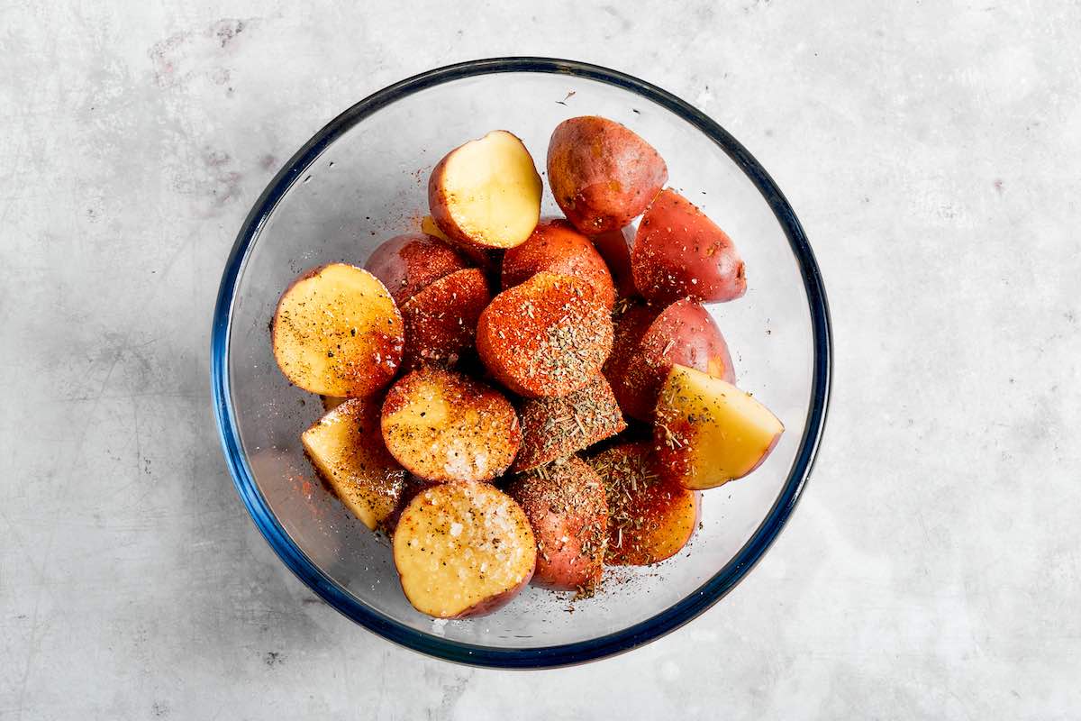 raw red potato halves with seasonings in a bowl.