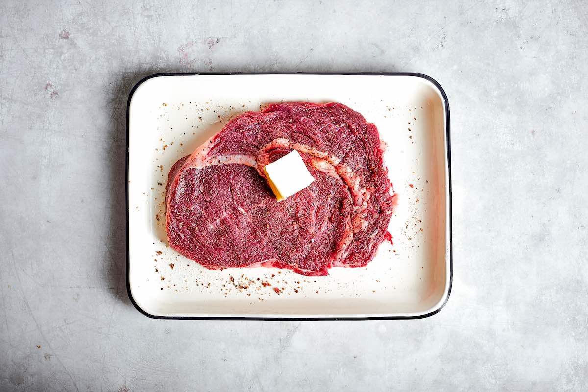 raw ribeye steak with a pat of butter on top.