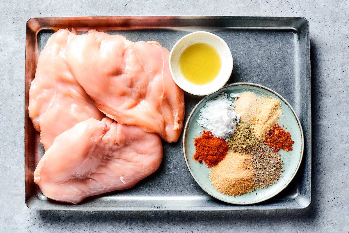 raw chicken breasts with seasoning in a bowl.