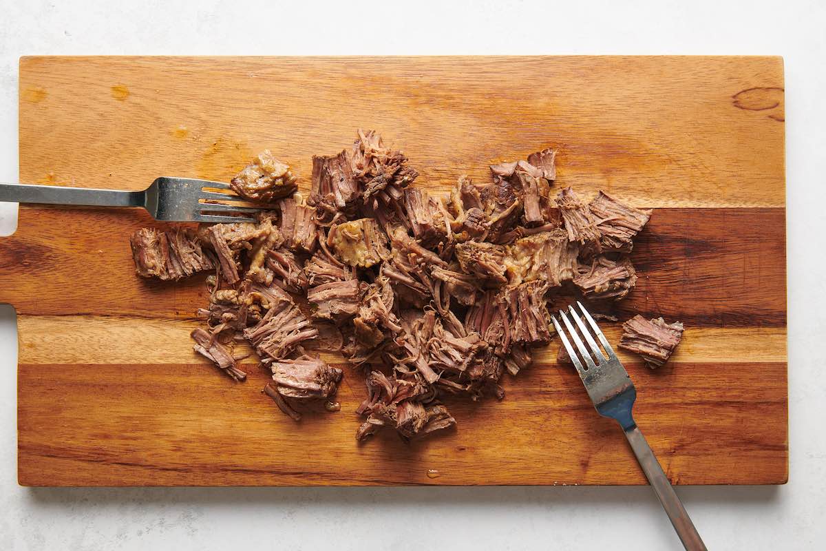 shredding beef with two forks on a wooden board.