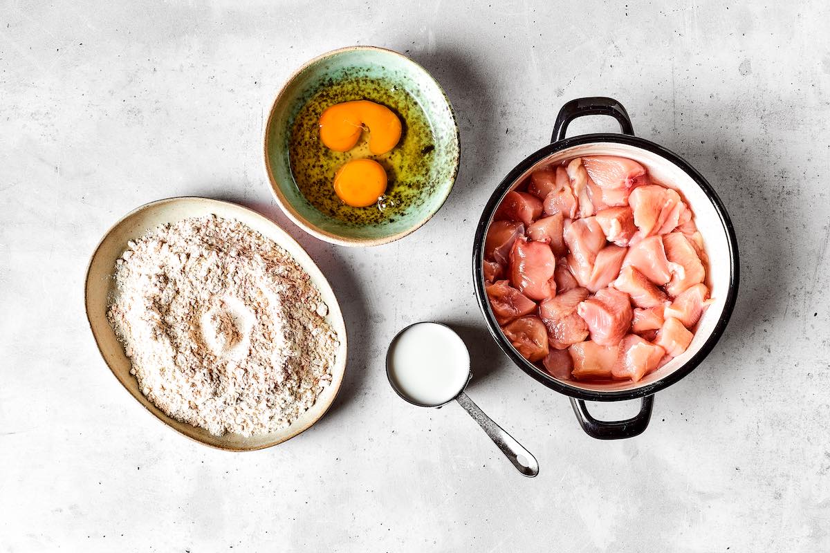 eggs in one bowl, flour in another bowl, and diced raw chicken.