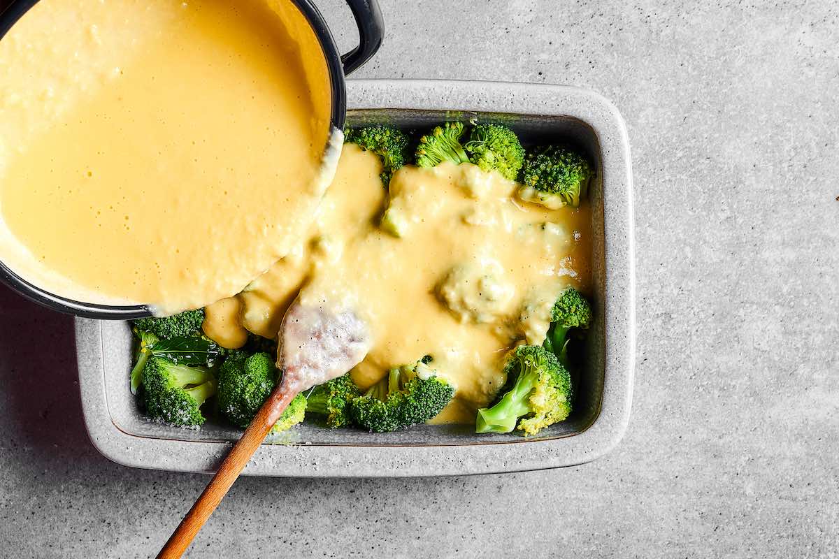 pouring cheese sauce over broccoli.