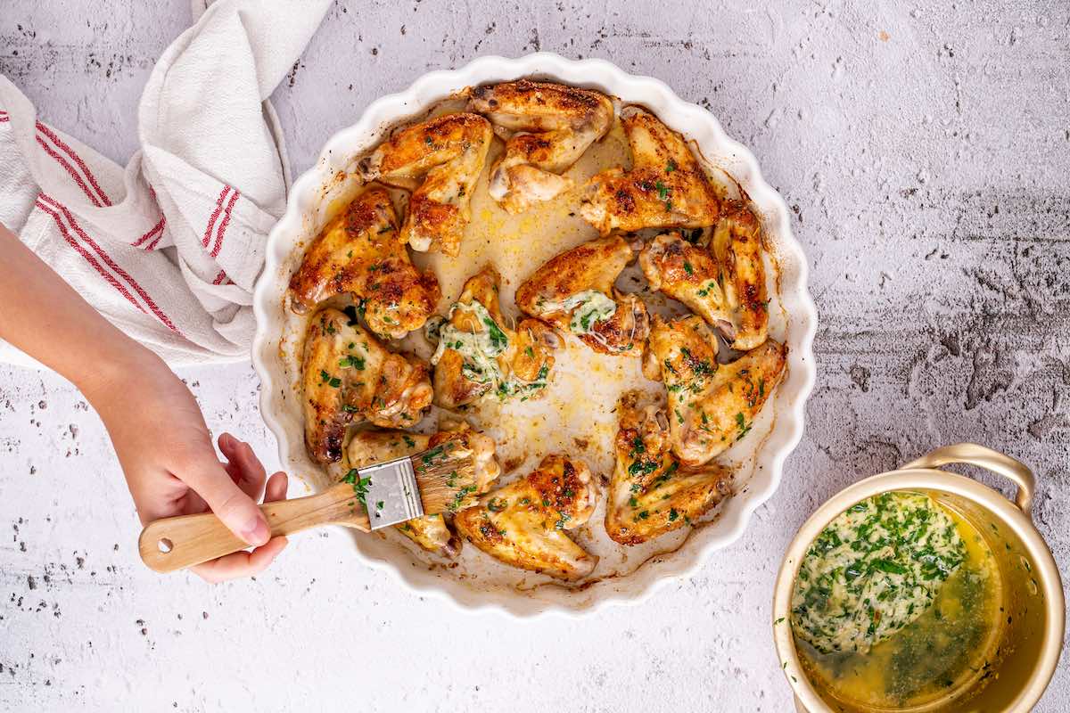 brushing garlic parmesan sauce on baked chicken wings.