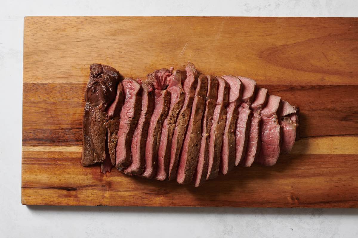 sliced london broil on a wooden board.